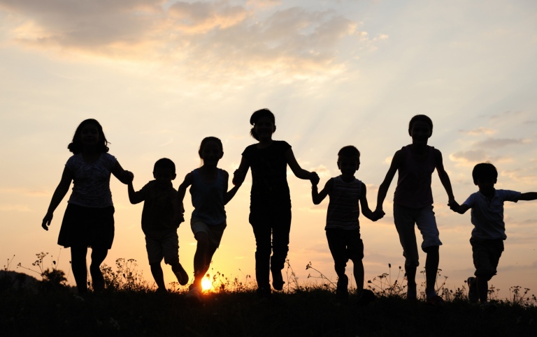 Siluetter av en grupp barn som håller varandra i handen i solnedgång. Foto: Mostphotos/Zurijeta