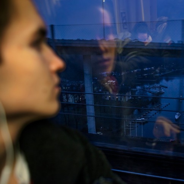 Kvinna tittar ut på ett landskap i skymning genom ett tunnelbanefönster.