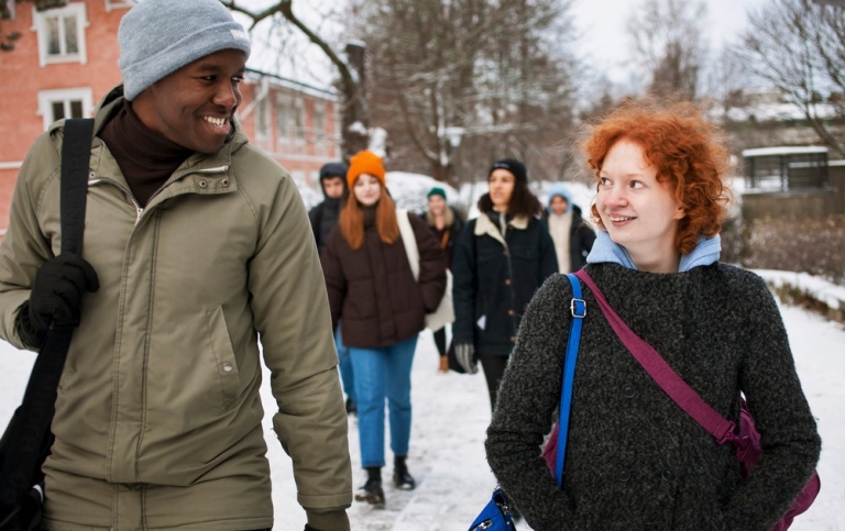 Leende studenter går på gångväg på vintrigt campus. 