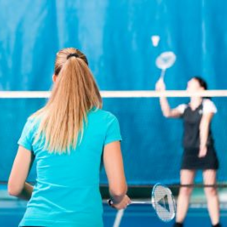 Kvinnor spelar badminton i en gymnastikhall.